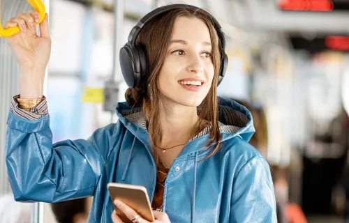 Female standing in a bus wearing headphones and looking out the window smiling
