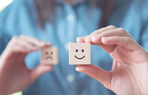 Woman holding two wooden dice, one with a smiley face and one with a sad face